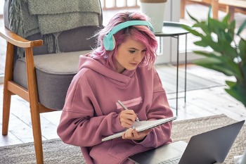 Eine junge Frau mit rosafarbenen Haaren absolviert mithilfe eines Tablets ein Pflegestudium als Fernstudium